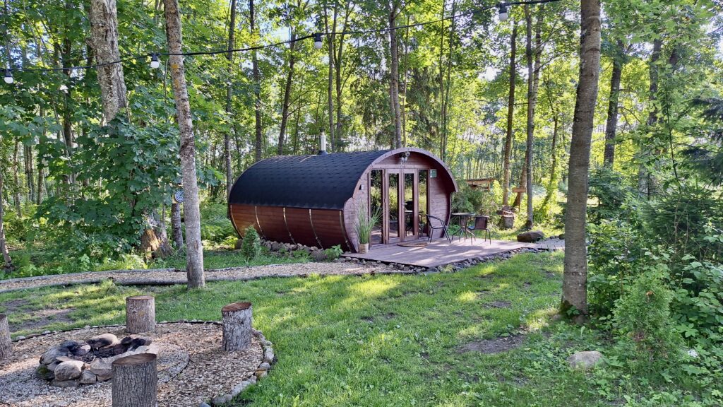 Wood-fired cabin with curved, barrel-shaped exterior in a forest, string lights above, and a small outdoor seating area on a wooden deck.